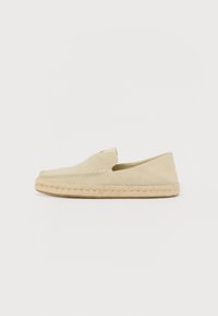 Zapato slip-on de espadrille en color beige claro, con una parte superior de lona texturizada y una suela de yute trenzado, que presenta una punta redondeada y detalles de costura mínimos.