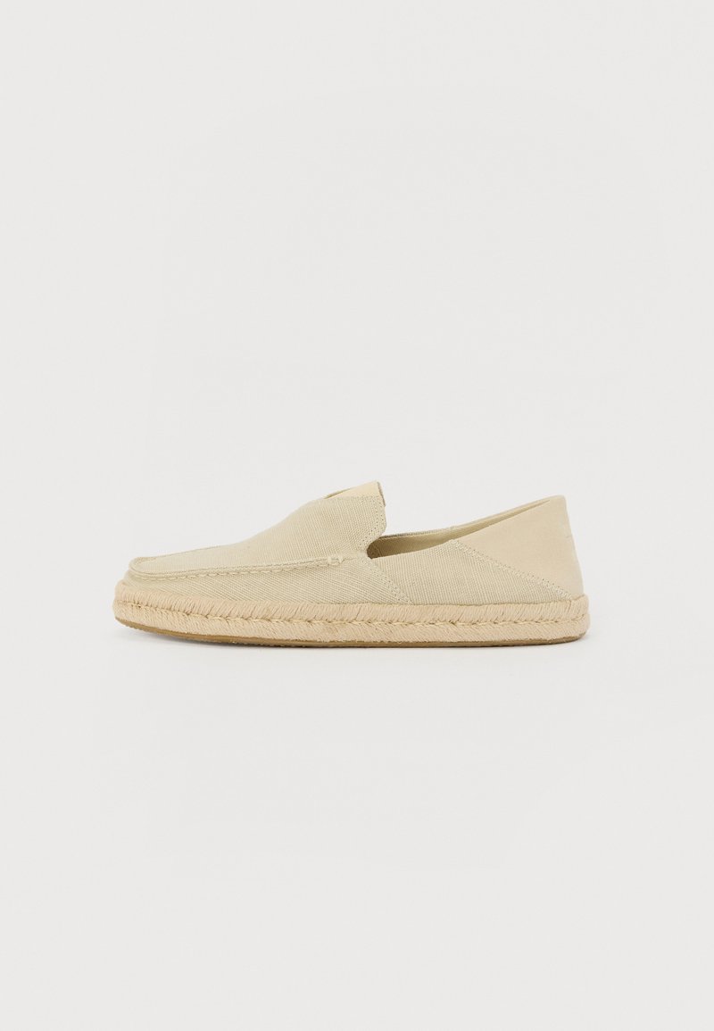 Zapato slip-on de espadrille en color beige claro, con una parte superior de lona texturizada y una suela de yute trenzado, que presenta una punta redondeada y detalles de costura mínimos.