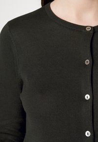Dunkelgrüne Strickjacke mit rundem Halsausschnitt, geripptem Muster und sechs passenden Knöpfen auf der Vorderseite. Nahaufnahme von Stoff- und Knopfdetails.
