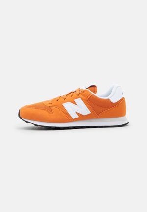 Oranger Sneaker mit niedrigem Schaft, weißem "N"-Logo, weißem Fersenriemen, weißem gepolstertem Kragen und schwarzer Gummisohle auf weißem Hintergrund.