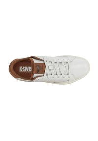 Zapatilla de piel blanca con acentos marrones, que presenta un diseño de cordones planos, detalles laterales perforados y una plantilla texturizada con logotipo.