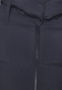 Dunkelblaue Steppjacke mit hohem Kragen, Frontreißverschluss und Druckknöpfen. Das Material wirkt glatt mit leicht glänzendem Finish.