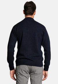Navy blue knitted sweater with a round neckline and ribbed cuffs and hem. Material appears soft and textured. Worn over gray trousers.