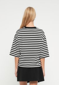 Μαυρολευκό ριγέ κοντομάνικο μπλουζάκι με στρογγυλή λαιμόκοψη και άνετη εφαρμογή, σε συνδυασμό με μαύρη φούστα.