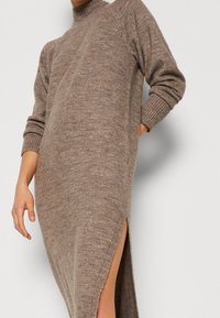 Robe pull en maille dans un mélange de laine douce marron, col montant, manches longues, avec des fentes latérales pour faciliter les mouvements. Poignets et ourlet côtelés.