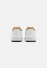 Baskets blanches avec une tige en mesh texturé beige, une semelle en caoutchouc blanc doux et un logo Lacoste discret sur le talon et sur le côté.