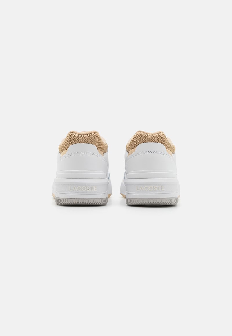 Weiße Sneakers mit einem strukturierten, tannfarbenen Mesh-Obermaterial, einer soft weißen Gummisohle und dezentem Lacoste-Branding an der Ferse und an der Seite.