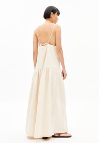 Maxikleid aus leicht beigem Stoff mit tiefem Rücken und verstellbaren Trägern, einem gerafften Rock und kontrastierenden Nahtdetails.