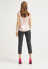 Vaaleanpunainen satiininen ilmanhiha toppi, jossa on napit, yhdistettynä tummanharmaisiin lyhyisiin housuihin ja kirkkaanpunaiseen korkokenkiin.