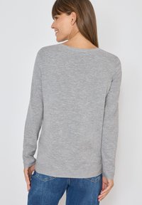 Maglione grigio a maniche lunghe in un morbido tessuto lavorato. Presenta un collo rotondo e una vestibilità rilassata, abbinato a jeans in denim blu.