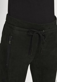 Svarta mockajoggers med justerbart midjeband, dragsko-stängning och sidsfickor med dragkedja. Slät struktur och minimalistisk design.