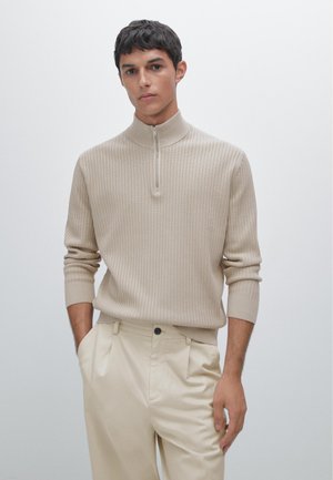 Beige ribbed pullover with a high collar and half-zip closure. Paired with cream pleated trousers. Smooth texture and fitted design.