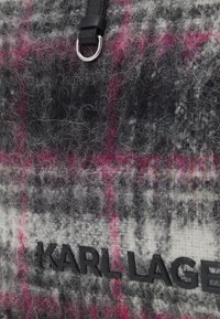Håndtaske i uldblanding med et gråt og pink ternet mønster, prægede sorte logo og en læderrem med en metalring.