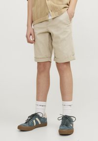 Beige short met omgeslagen mouwen van katoen twill met zijzakken. Gepaarde met donkerblauwe sneakers, witte sokken en een gebreide beige cardigan.