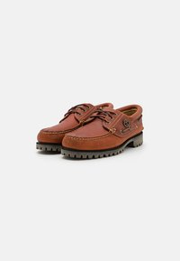 Brown leather shoes with a low profile, round toe, contrasting white stitching, lace-up design, and textured rubber sole.