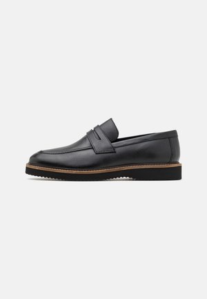 Chaussure en cuir noir à enfiler avec un bout rond, un double dessus à sangle et une semelle marron contrastante. Fini texturé avec une apparence lisse.