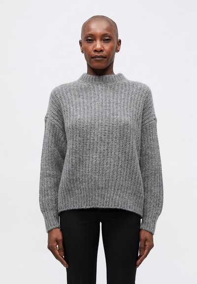 Pull en tricot gris avec un col haut, coupe ample et texture côtelée. Doté d'épaules tombantes et de manches longues. Associé à un pantalon noir.