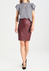 Randig kortärmad blus med nyckelhålskrage, kombinerad med en figurnära bordeaux läder blyertkjol, bärs med svarta högklackade skor.