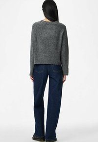 Pelēks īss džemperis ar viļņotu apakšmalu, apvienots ar tumši zilām platām džinsa biksēm, kas izceļas ar teksturētu audumu un minimālistisku dizainu.