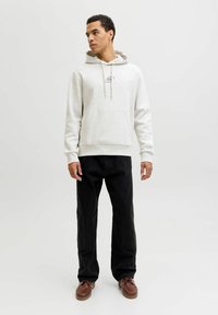 Sweat à capuche gris clair avec cordons ajustables, poche kangourou à l'avant, poignets et ourlet côtelés, assorti à un pantalon noir et des chaussures marron.