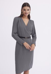 Czarna i biała sukienka w paski z fasonem kopertowym, długimi rękawami i dopasowaną sylwetką. Udekorowana czarnym paskiem i guzikami.