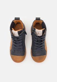 Zapatos de piel de color azul marino, de caña alta, con suelas de goma marrones, cordones y cremalleras laterales; detalles texturizados y cuello acolchado.