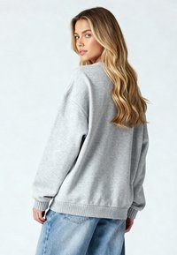 Harmaat collegepaita, jossa on rento istuvuus, kireät hihansuut ja helma. Kangas näyttää pehmeältä ja siinä on lievää tekstuuria. Yhdistetty sinisiin farkkuihin.