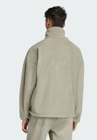 Fleece pullover in soft beige with a high collar, loose fit, and dropped shoulders. Features textured fabric and a curved hem.