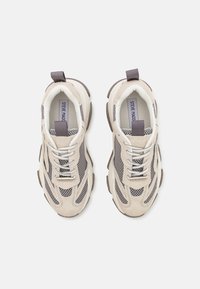 Beige sneakers with gray mesh upper, suede accents, textured sole, and contrasting gray laces and heel tabs. "STEVE MADDEN" logo inside.
