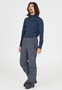 Herre navy langærmet base layer skjorte med kvart-zip, parret med grå snebukser med lynlåslommer og bælte. Sorte støvler vist.
