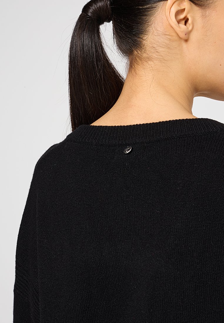 Maglione nero lavorato a maglia con scollo rotondo e un piccolo dettaglio metallico sul retro. Tessuto morbido con un design a vestibilità ampia.
