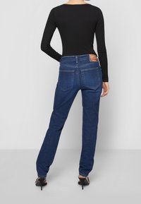 Jeans in denim di un blu profondo con un taglio dritto. Le caratteristiche includono due tasche posteriori e un'etichetta sulla vita. Indossati con un top nero.