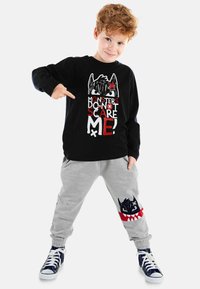 Schwarz langärmliges Shirt mit Monstergrafik in Weiß und rotem Text, kombiniert mit grauen Jogginghosen, die ein schwarzes Monstergesicht und rote Akzente aufweisen.