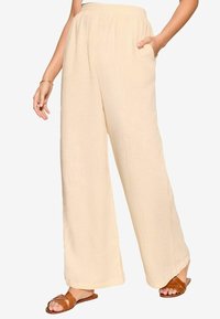 Světle béžové široké kalhoty vyrobené z texturované látky s elastickým pasem a bočními kapsami. Doplněné hnědými nazouvacími sandály.