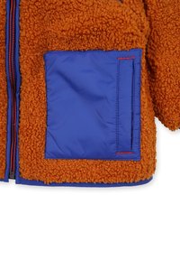 Fleecejack met oranje gestructureerde buitenkant, blauwe geïsoleerde voering, contrasterende panelzak en rode stiksels langs de rits.