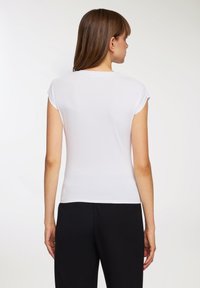 Biała krótko-sleeve dopasowana koszulka z podwiniętymi rękawami, gładka w fakturze, z okrągłym dekoltem, zestawiona z czarnymi spodniami.