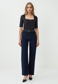 Zwarte top met vierkante hals, gecombineerd met high-waisted donkerblauwe brede jeans met voorzakken en een smalle riem met een zilveren gesp.
