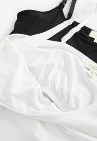 Drie tanktops gestapeld: een witte met gathered elastiek en een zwarte met verstelbare bandjes. Beide zijn gemaakt van zachte stof.