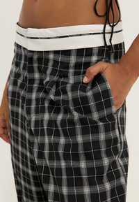 Svart och grå rutiga byxor i vävt tyg, med en vit midja och sidoficka, som har en slät yta och avslappnad passform.