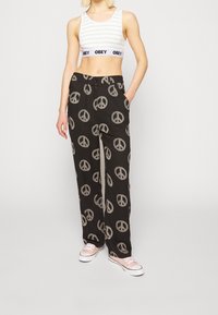 Schwarze weite Hosen mit einem weißen Friedenssymbol-Muster, kombiniert mit einem kurzärmligen Crop-Top in Weiß und Grün sowie hellrosa Sneakers.