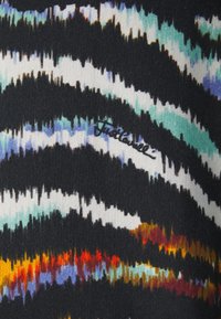 Tejido de punto con dinámicas rayas en zigzag en negro, blanco, verde azulado y naranja. Incluye texto bordado en negro. Textura suave, material elástico.