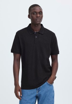 Sort polo-shirt med korte ærmer, tre-knaps lynlås og subtilt tekstureret stof. Bæres med lyseblå denimjeans.