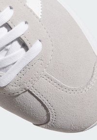 Jasnoszare zamszowe sneakersy z białymi sznurówkami, z przeszytymi akcentami i gładką teksturą. Okrągły czubek i subtelne elementy designu.