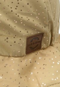 Chapeau bucket vert clair avec des motifs de cœurs métalliques. Fabriqué en tissu à la texture lisse. Présente un patch de logo brun sur le côté.