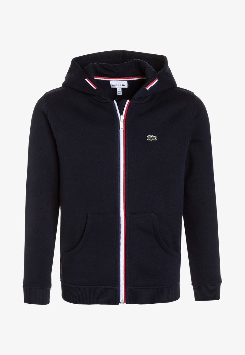 Tummansininen vetoketjullinen huppari, jossa on valkoiset ja punaiset raidat, kenguru-taskut ja vihreä brodeerattu logo vasemmassa rinnassa. Teksturoitu kangas.