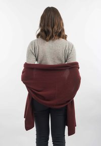 Burgundská šála obtočená kolem ramen, vyrobená z měkkého materiálu, s volně visící tkaninou a pohodlným střihem, doplněná světlou šedou blůzou.