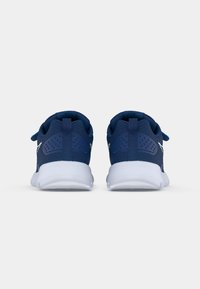 Baskets de sport bleu marine avec un matériau en maille texturée, semelle blanche, col rembourré et perforations sur les côtés pour la ventilation.