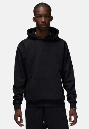 Sudadera negra con bolsillo canguro, capucha con cordón y logo "AIR JORDAN" en relieve en el frente. La tela parece suave y texturizada.
