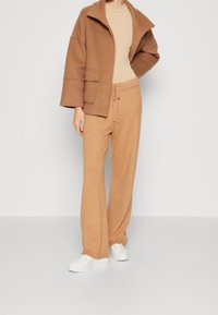 Brun uldblandingsjakke med oversized krave og forlommer, parret med lys brun vide bukser og hvide sneakers.