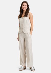 Ensemble beige clair en lin composé de deux pièces avec des rayures verticales, un gilet boutonné et un pantalon large. Des sabots en argent complètent le look.